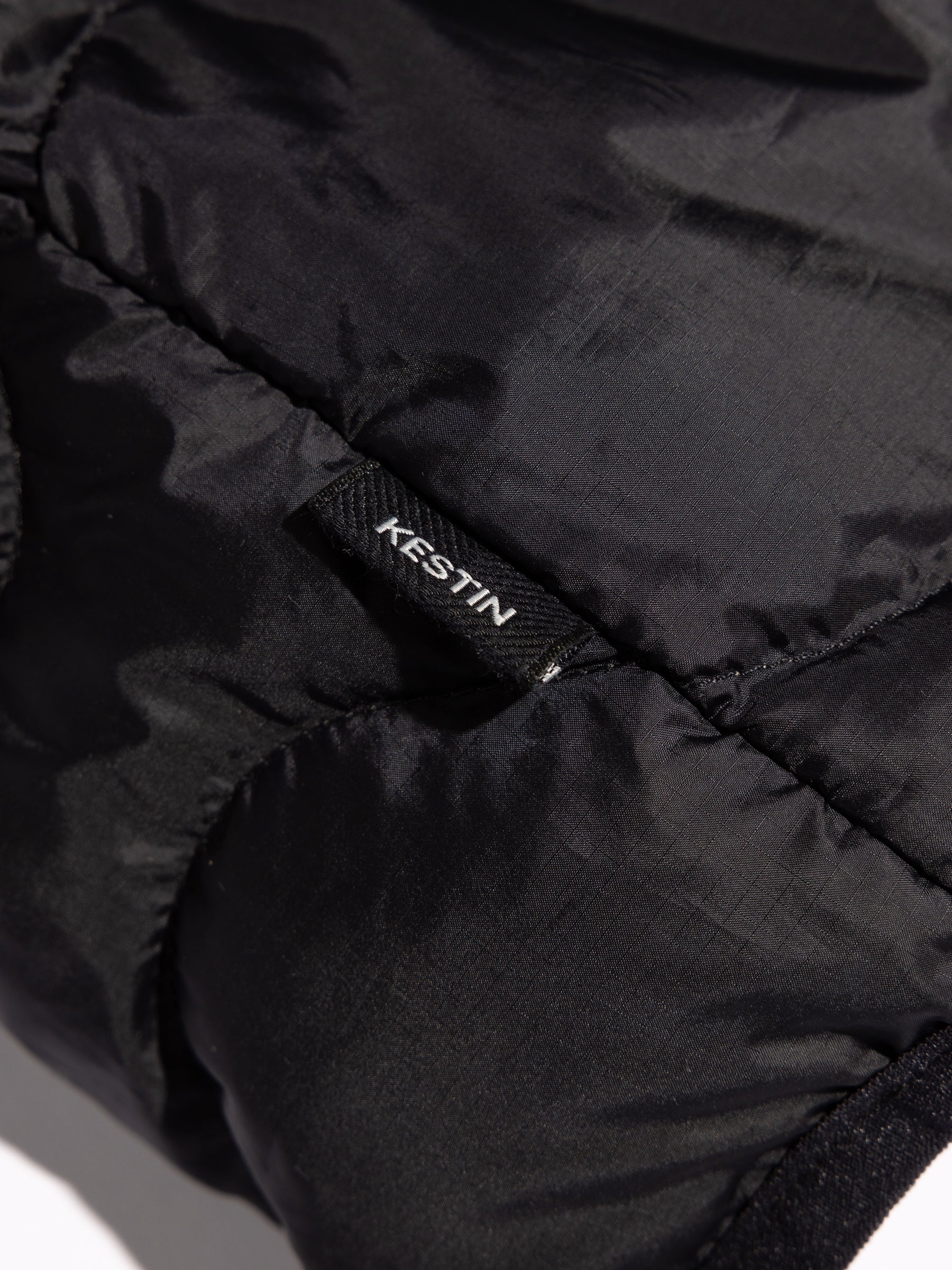 A woven flag label to the side of the KESTIN Cuillin Down Vest in black.