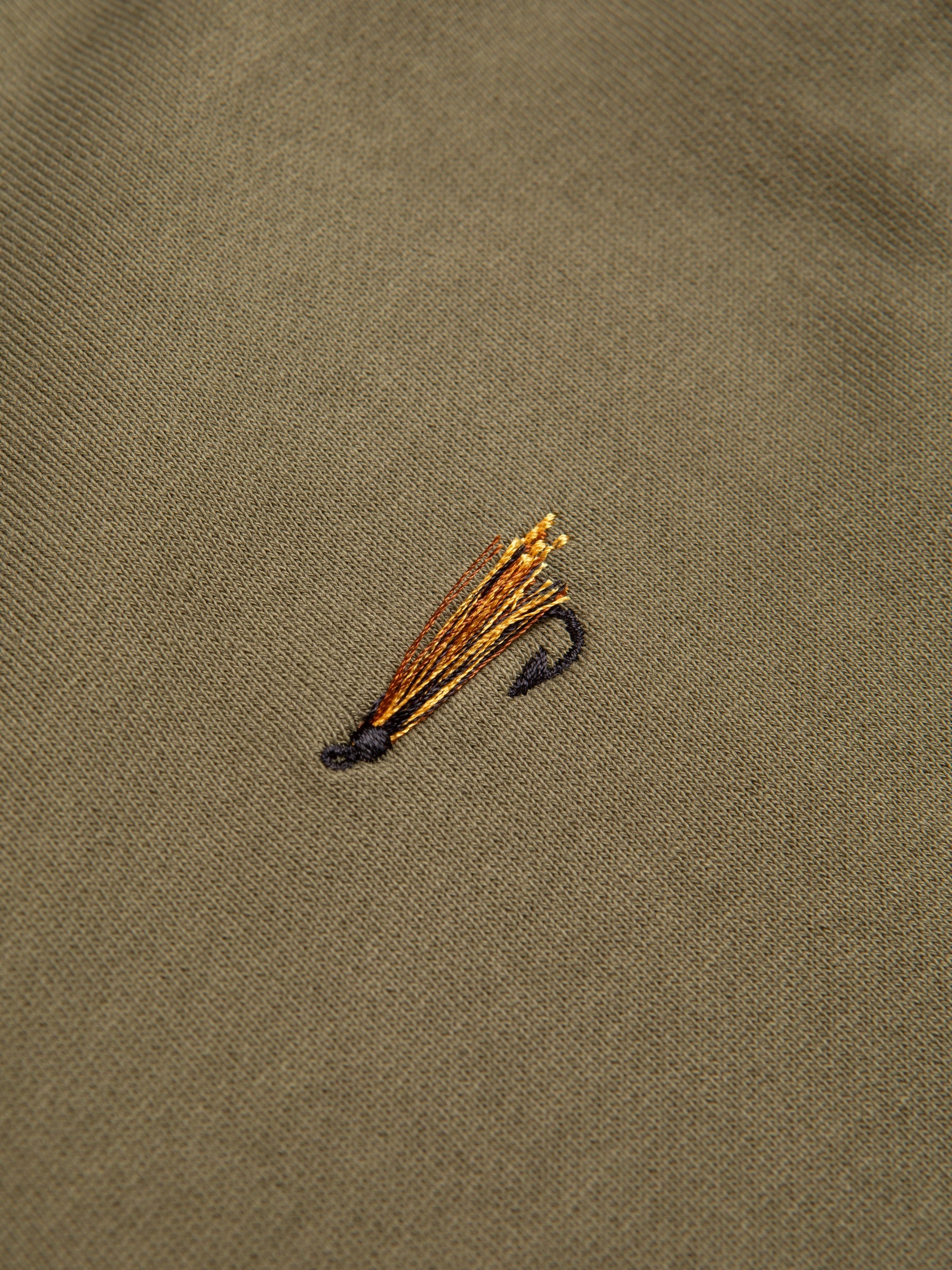 An embroidered fishing fly to the chest of an olive green sweatshirt.