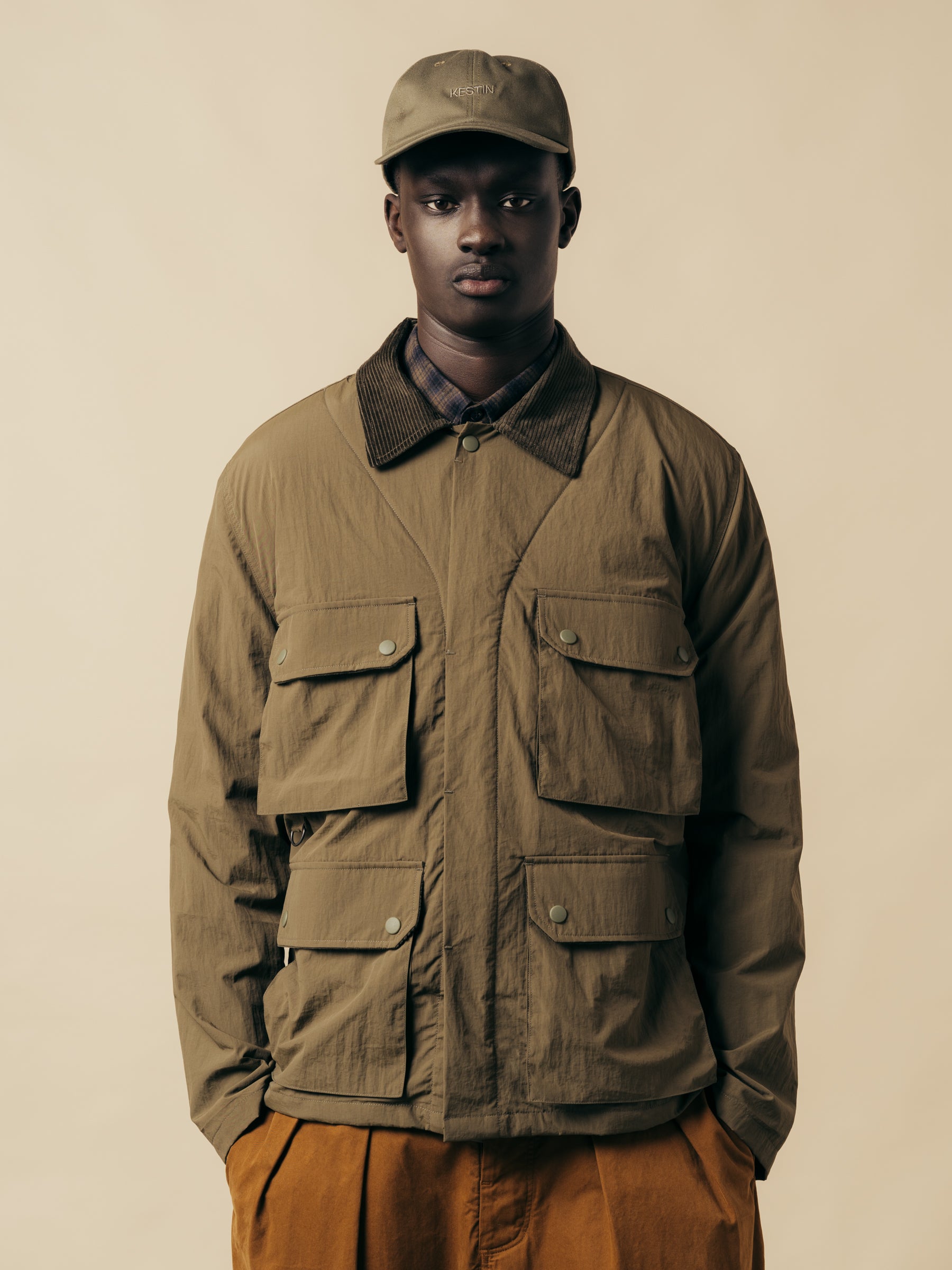 A model wearing a green country style jacket along with brown trousers and a green cap.