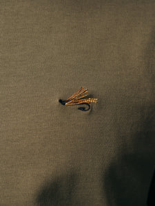 An embroidered fishing fly to the chest of an olive green t-shirt.