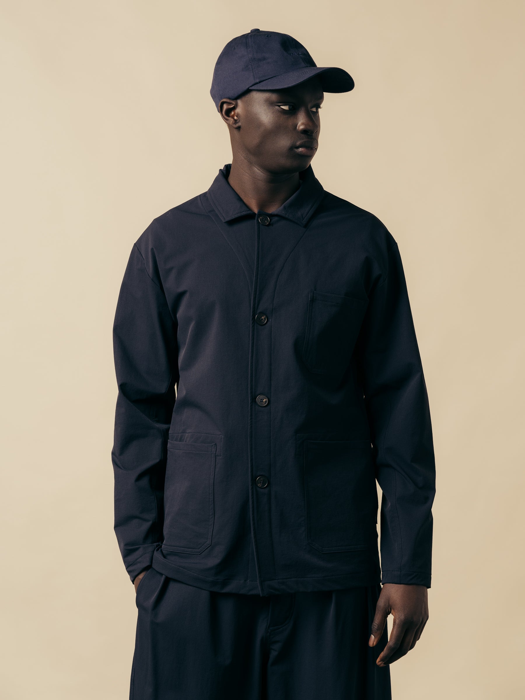 A model wearing a technical navy blue jacket, with matching pants and a cap.