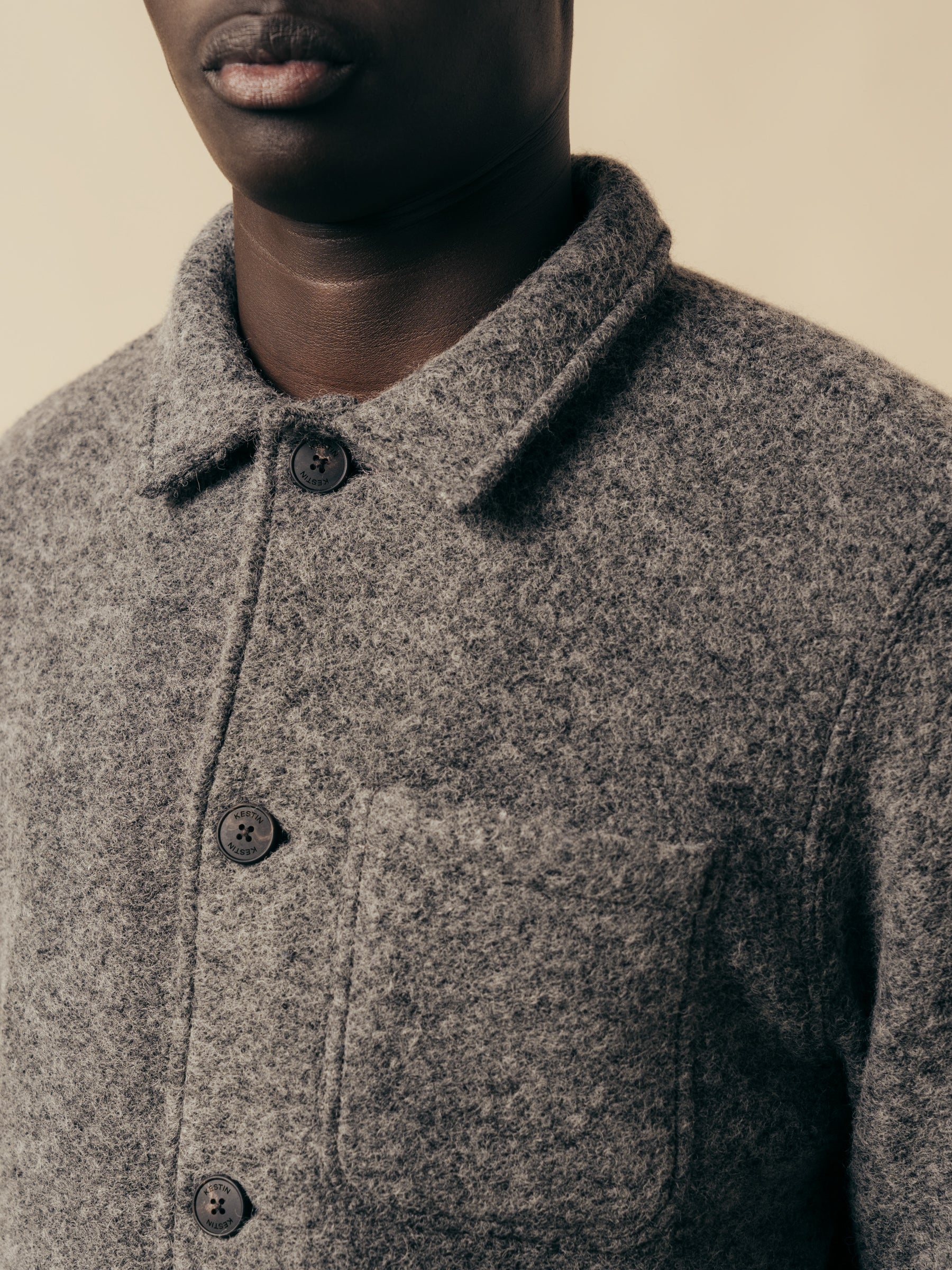 A close-up of the buttoned front and collar of a grey wool jacket, on a model.