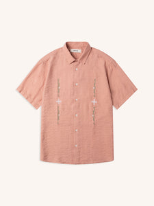 A pink short sleeve shirt in pink with embroidered artwork, on a white background.