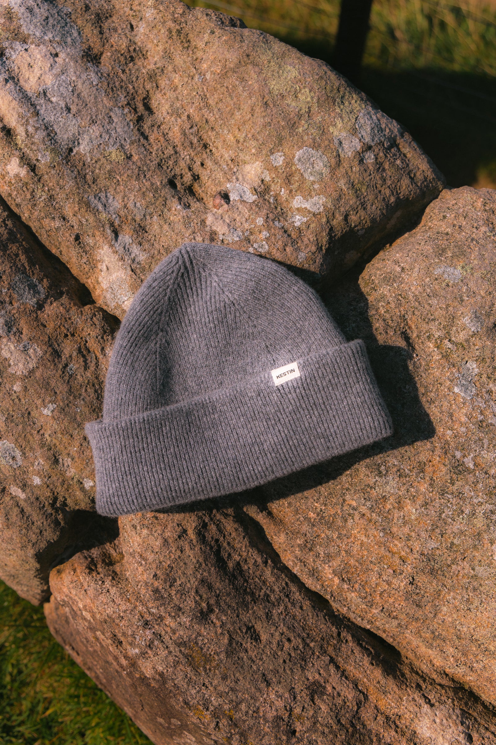 A grey beanie, knitted in Scotland, sitting on a rock.