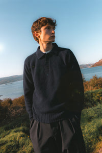 A model wearing a navy blue knitted polo, made in Scotland.