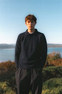 A man wearing a knitted polo sweater in navy blue, made in Scotland.