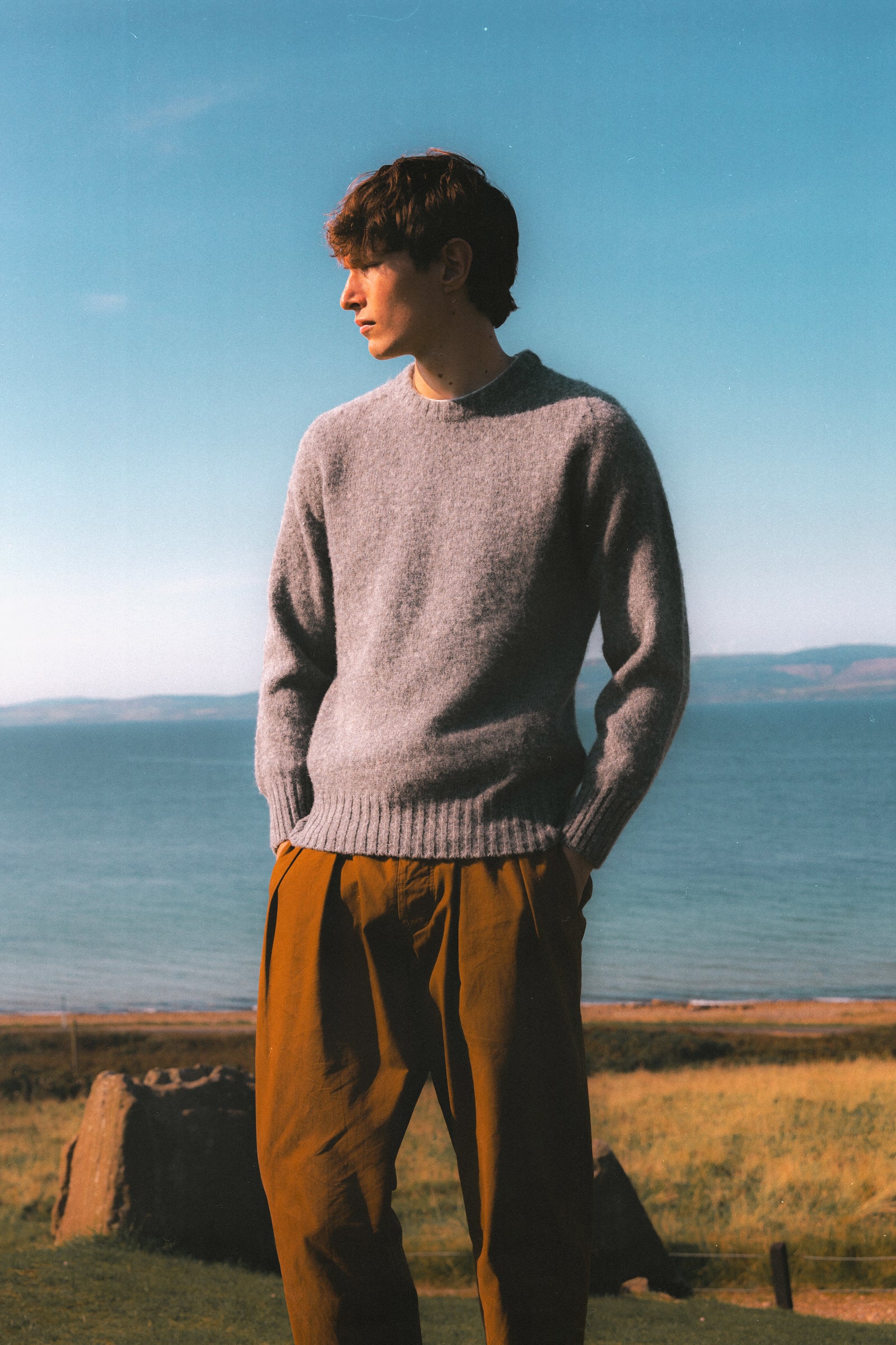 A model wearing a Made In Scotland knitted sweater in grey.