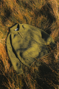 A green shetland wool polo shirt, pictured in some grass on the Isle of Arran.