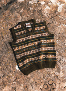 A Fairisle Sweater Vest in olive green, lying on a rock in Scotland.