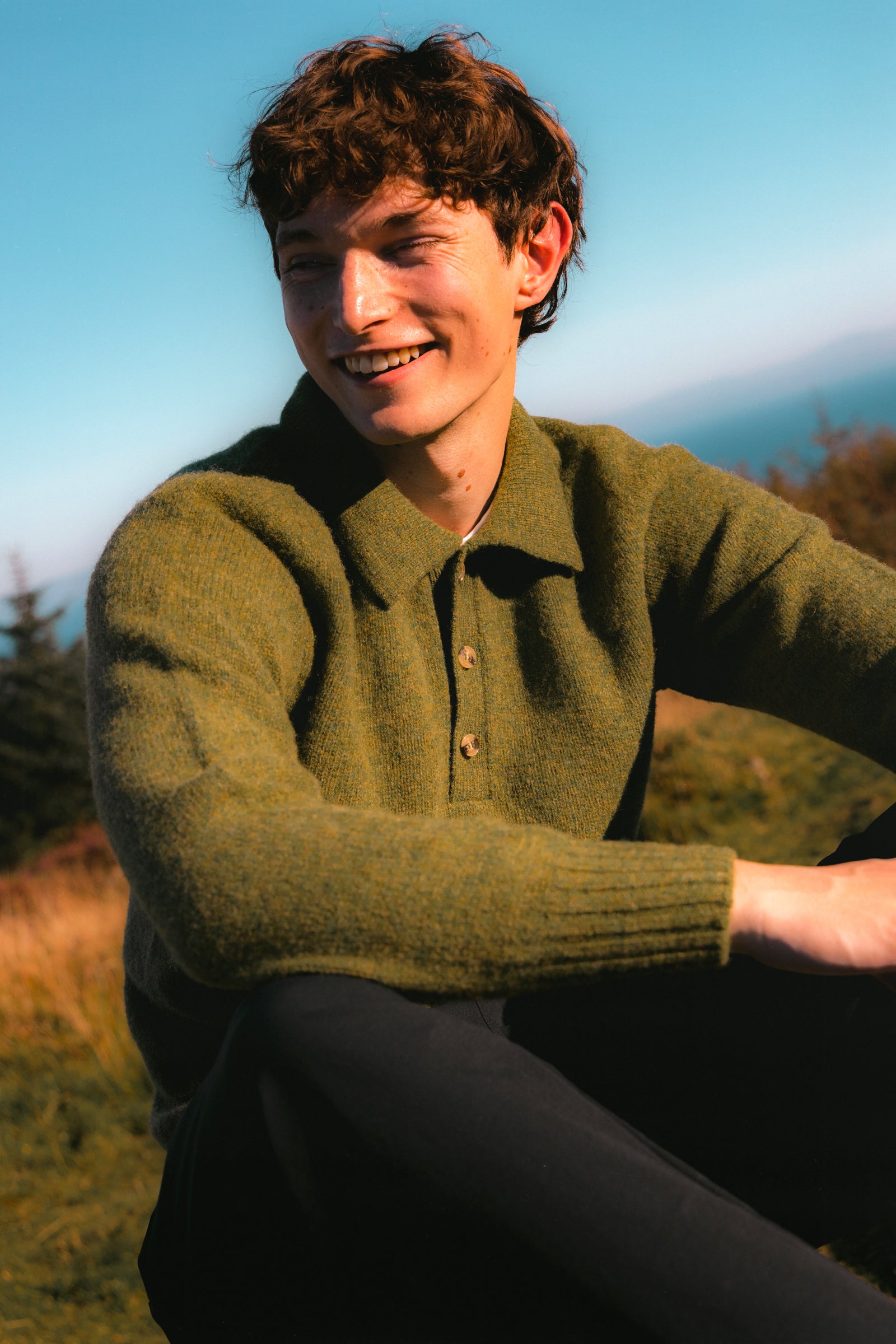 A model wearing a green knitted polo sweater, on the Isle of Arran.