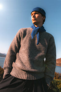 A model wearing a grey sweater and a blue beanie and bandana, made in Scotland.