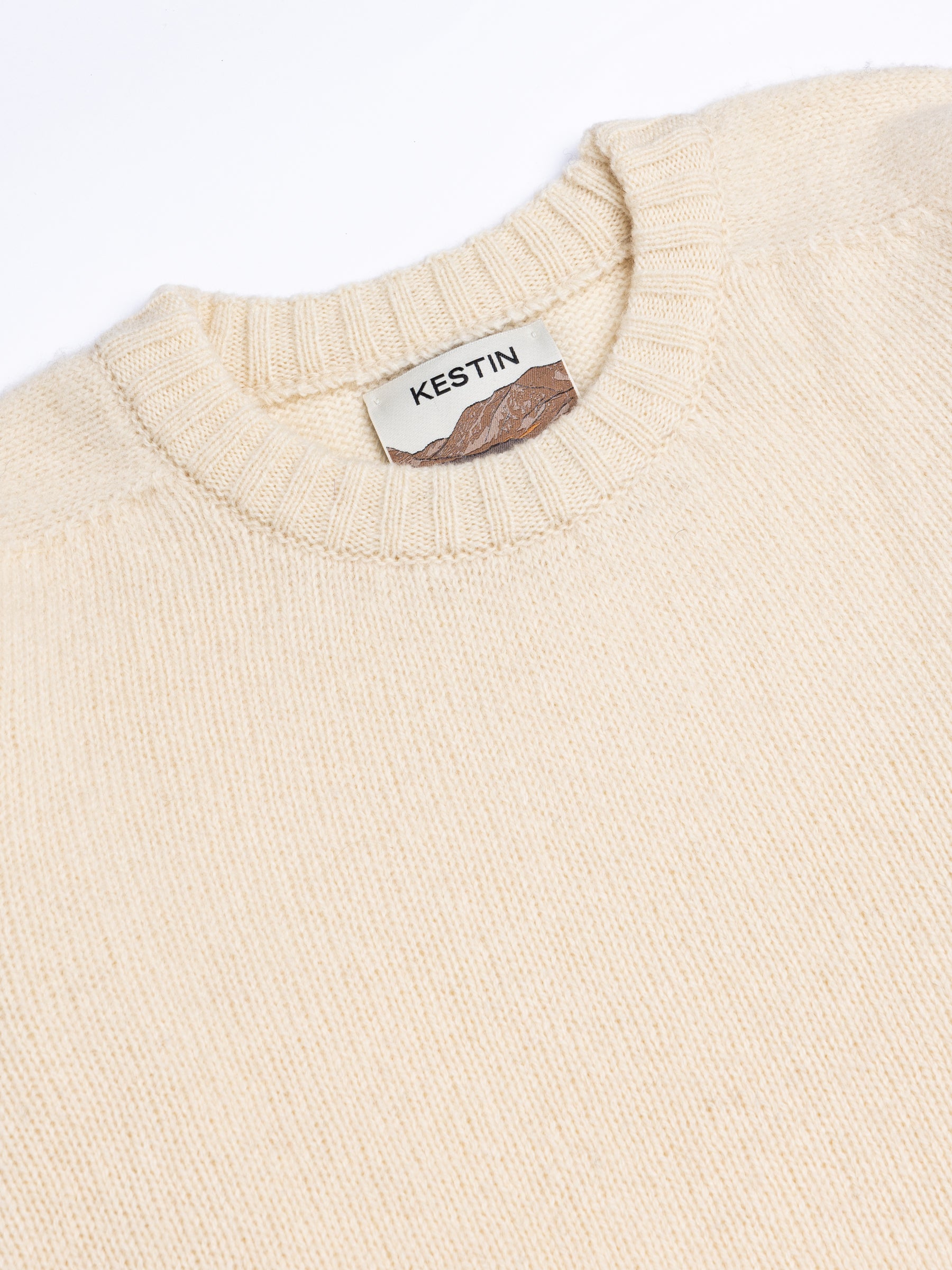 A close-up of the crew neck to a Shetland wool sweater, in cream.