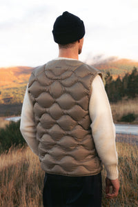 A man wearing a green down gilet over a cream knitted sweater.