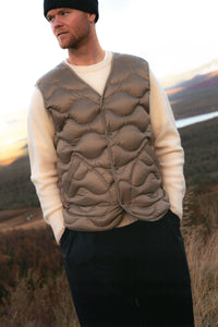 A man wearing a down insulated vest over a knitted wool sweater.