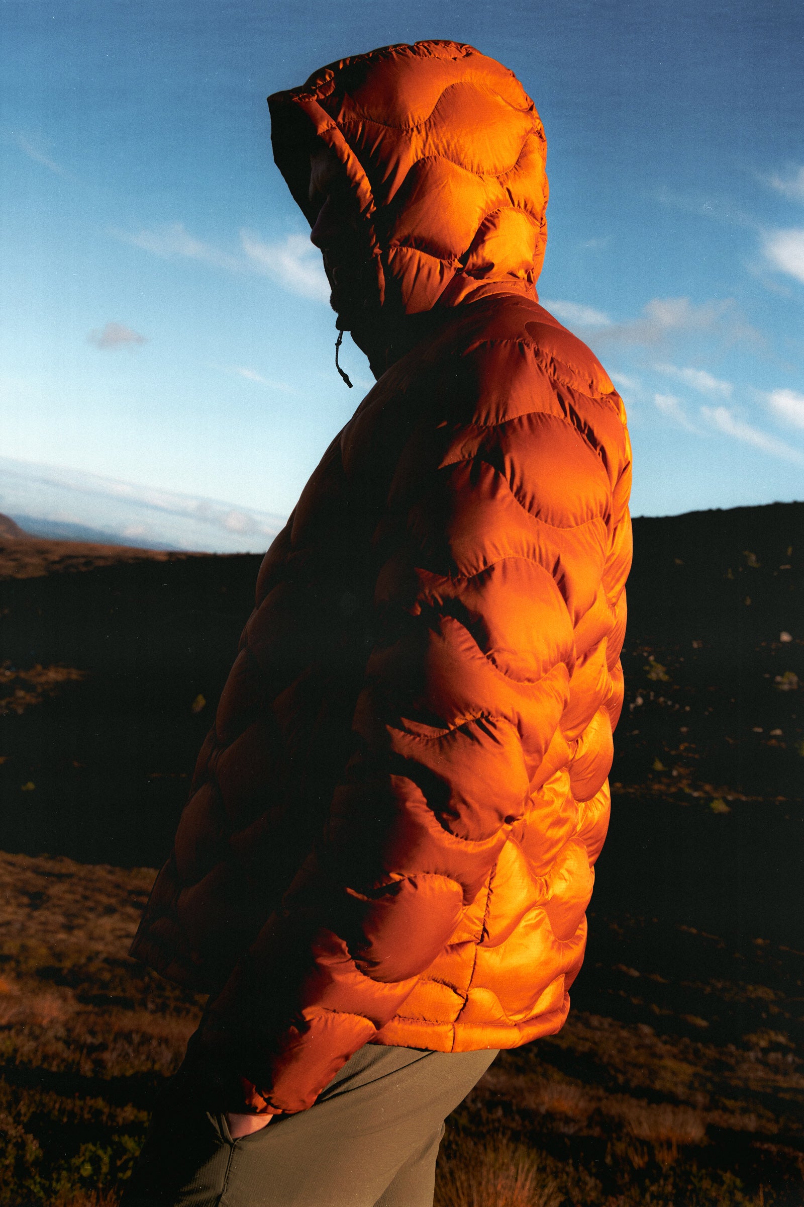 A man wearing an orange down jacket during sunset in Scotland.