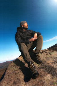 A man wearing a black down jacket, hiking pants and leather boots.