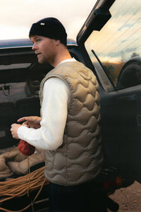 A man wearing a down insulated vest in green, getting rock climbing gear out of a car.