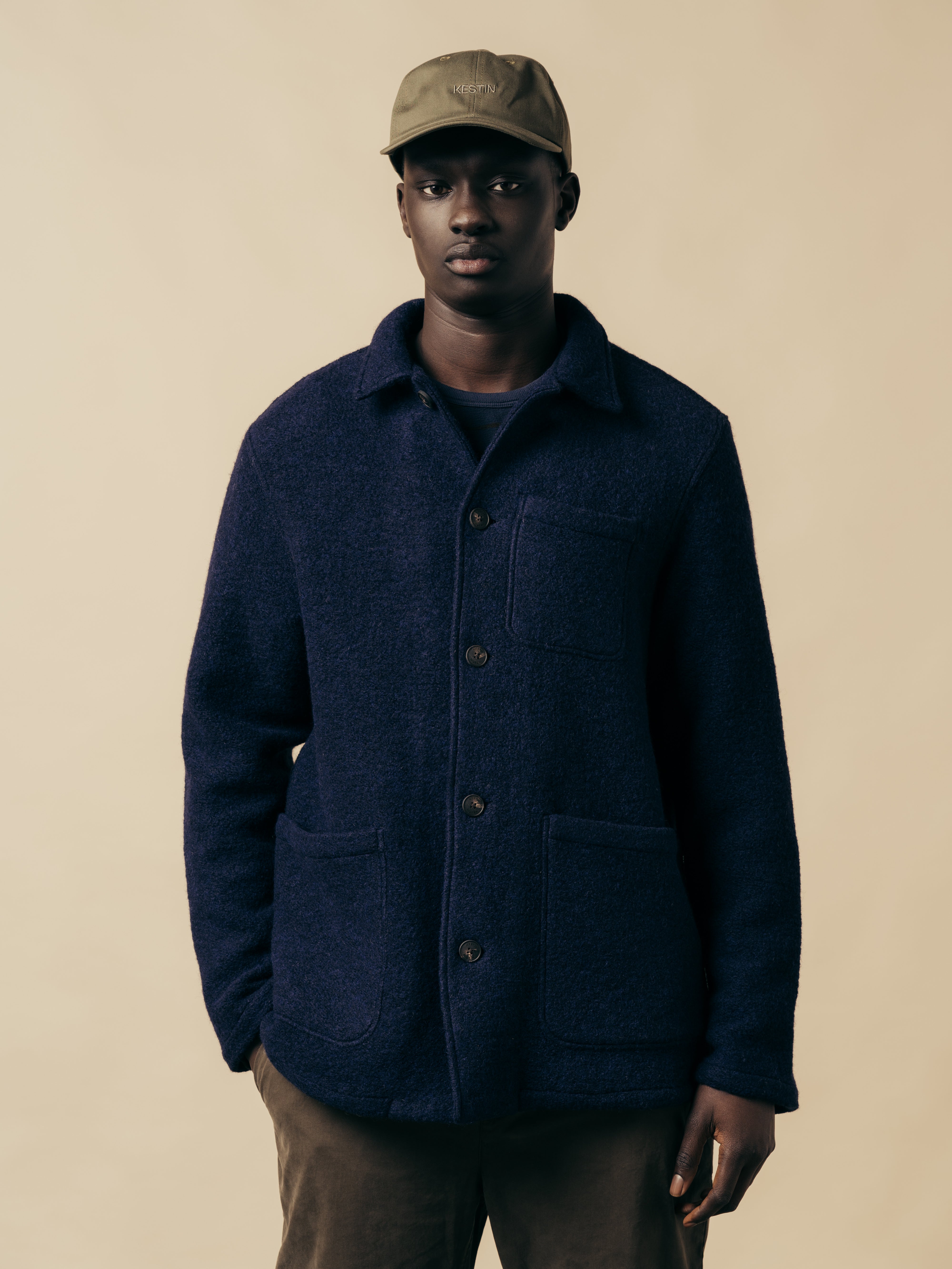 A model wearing a navy blue wool fleece jacket, with a green cap and trousers.