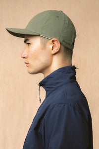 A model wearing a navy zip neck jacket and olive green cap.