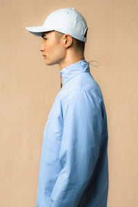 A model wearing a bright blue zip neck and a cap from menswear brand KESTIN.