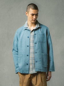 A blue chore coat layered over a check shirt, worn with tan trousers.